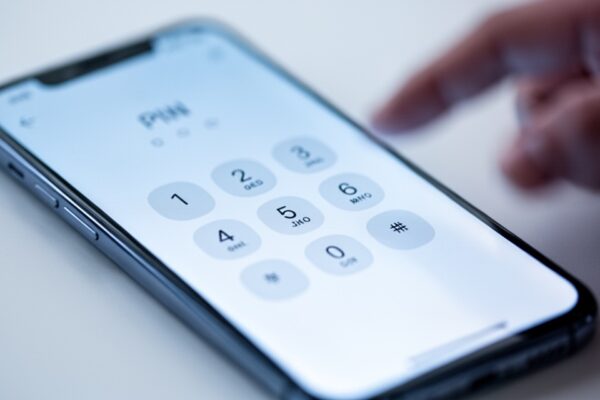 Ekran smartfona z interfejsem wprowadzania kodu PIN i klawiaturą numeryczną, dłoń wskazująca na ekran